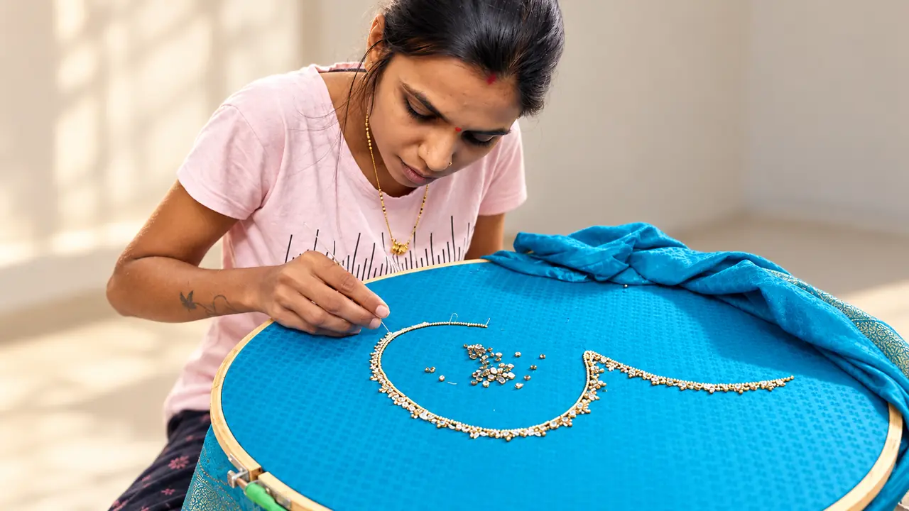 SACH Couture artisan applying gold neckline detailing to turquoise fabric on an embroidery frame