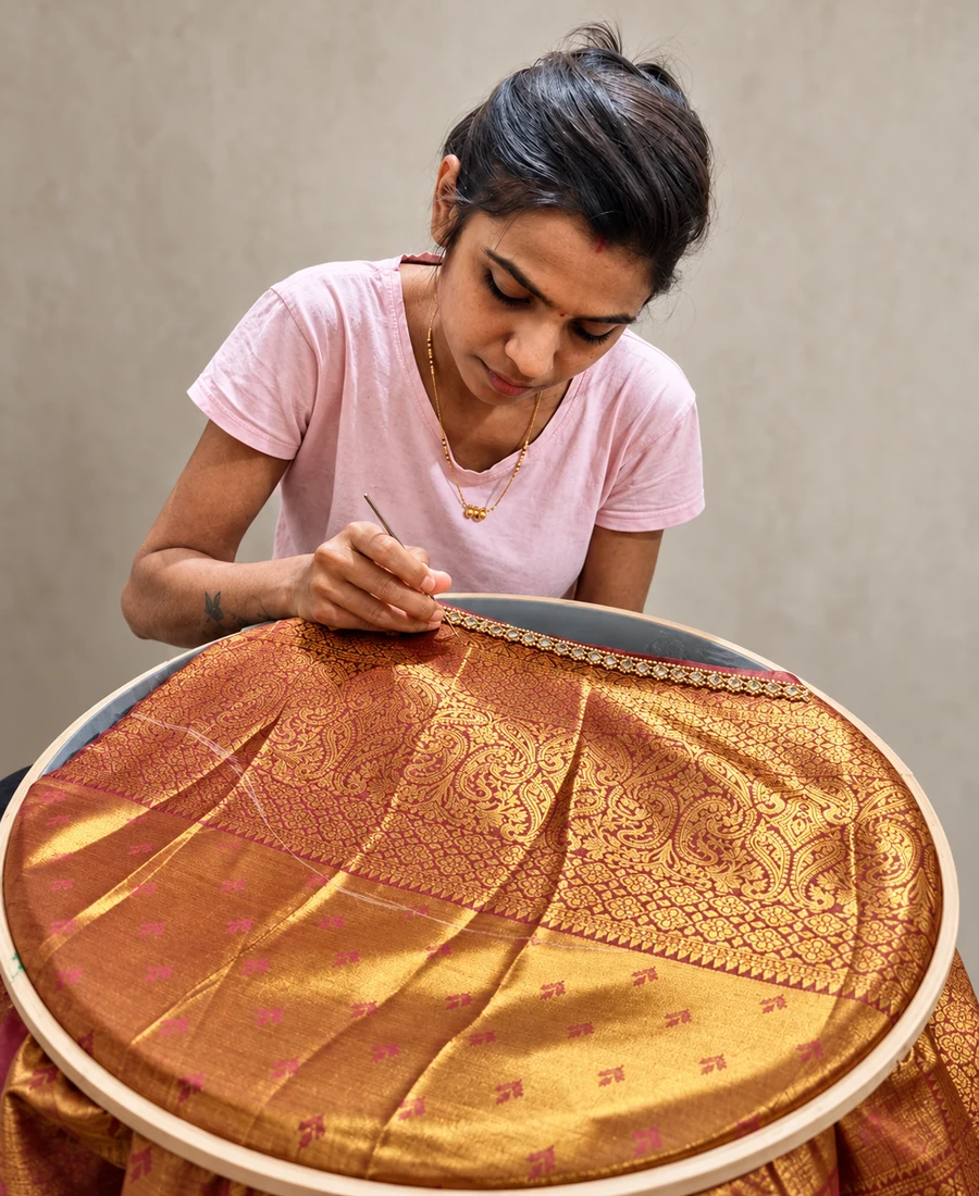 Pranali working on an embellished border on maroon-and-gold brocade in an embroidery frame at SACH Couture.