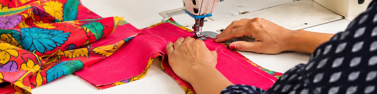Close-up of guiding pink garment fabric through a sewing machine at SACH Couture.