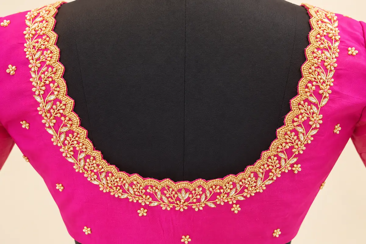 Close-up of a pink blouse's deep U-shaped back neckline with scalloped gold floral embroidery and stone detailing, by SACH Couture.